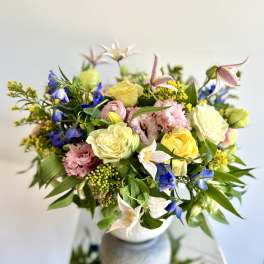 Mixed bouquet of pastel roses, blue flowers, and pink blooms in a vase