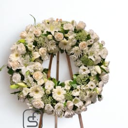 Large white and cream floral wreath with roses, lilies, and gerbera daisies on a wooden easel.
