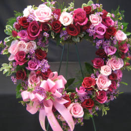 Heart-shaped rose wreath with pink ribbon bow on a stand
