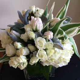 White roses and hydrangeas in a square glass vase with variegated leaves