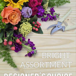 Bright mixed bouquet with roses, sunflower, and purple blooms beside pruning shears