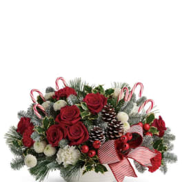 Christmas arrangement with red roses, pinecones, and candy canes in a white bowl