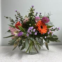 Mixed bouquet in a clear glass vase with orange, pink, and purple flowers