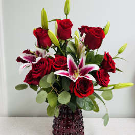 Red roses and pink lilies in a dark glass vase