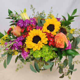 Bouquet of sunflowers, peach roses, and purple flowers in a glass vase