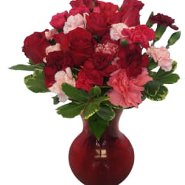 Red and pink carnations with roses in a red glass vase