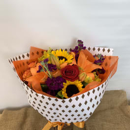 Bouquet of sunflowers, roses, lilies, and purple flowers wrapped in patterned paper