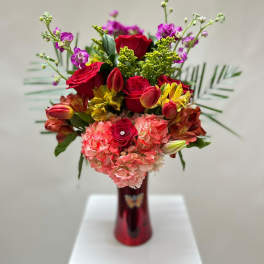 Mixed bouquet of red roses, pink hydrangeas, and yellow flowers in a red vase