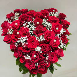 Heart-shaped bouquet of red roses with baby's breath in a white vase