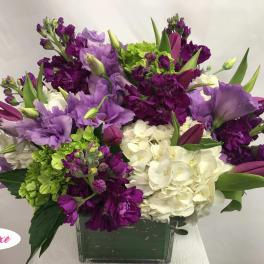 Purple and white floral arrangement in a square glass vase