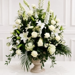 White floral arrangement with roses and lilies in a stone pedestal vase