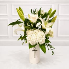 White lilies and hydrangea in a white vase with a cross emblem