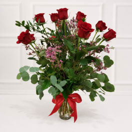 Red roses in a glass vase with pink filler flowers and a red ribbon
