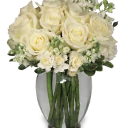 Round arrangement of white roses and white flowers in a clear glass vase