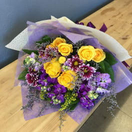 Bouquet of yellow roses and purple flowers wrapped in lavender paper