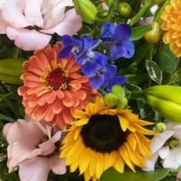 Bright mixed bouquet with sunflowers, orange blooms, pink lisianthus, blue delphinium, and lily buds.