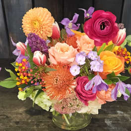 Colorful mixed bouquet in a clear glass vase with roses, tulips, and dahlias