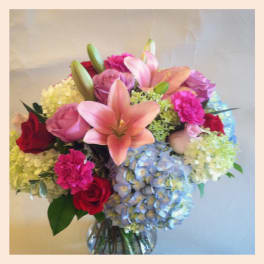 Mixed bouquet of pink lilies, roses, carnations, and hydrangeas in a clear glass vase