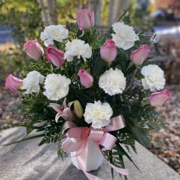 Pink roses and white carnations in a white vase with a pink ribbon