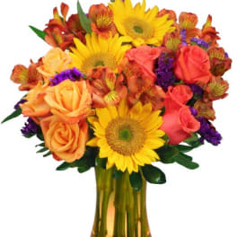 Bright arrangement of yellow sunflowers, orange roses, and purple accents in an amber glass vase