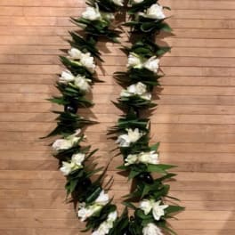 White floral lei with dark green leaves on a wooden floor