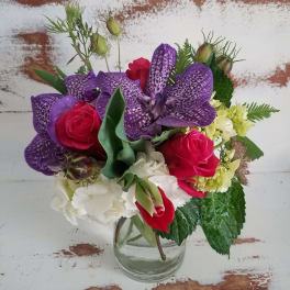 Bouquet of purple orchids, red roses, and white hydrangea in a clear glass vase