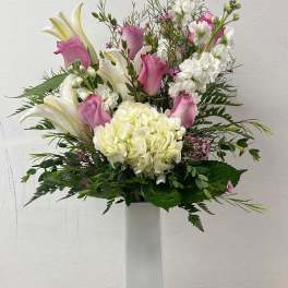 Pink roses and white lilies arranged in a tall white vase