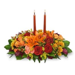 Low centerpiece of orange lilies, red and peach roses with two tall orange taper candles