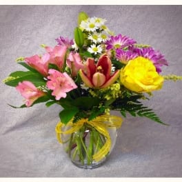 Mixed bouquet of pink, yellow, and purple flowers in a glass vase