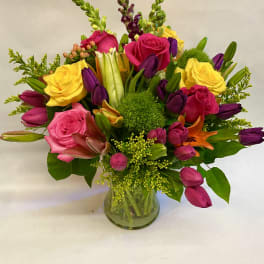 Mixed bouquet of roses, tulips, lilies, and snapdragons in a glass vase