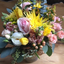 Mixed bouquet of pink roses, yellow blooms, and white flowers in a glass vase