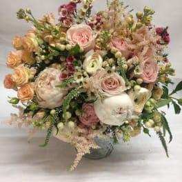 Blush and cream bouquet of roses, peonies, and small filler flowers in a glass vase.