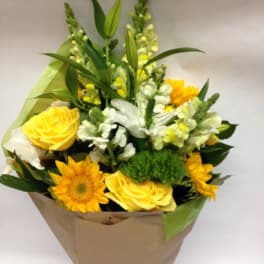 Bouquet of yellow roses, sunflowers, and white snapdragons wrapped in paper