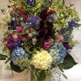 Mixed bouquet with hydrangeas, calla lilies, and delphinium in a glass vase