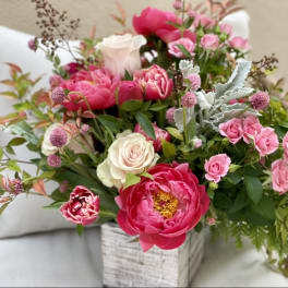 Pink peonies and roses arranged in a whitewashed wooden box