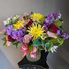 Mixed bouquet of yellow, purple, pink, and red flowers in a glass vase