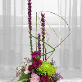 Tall floral arrangement with purple and pink blooms in a low container