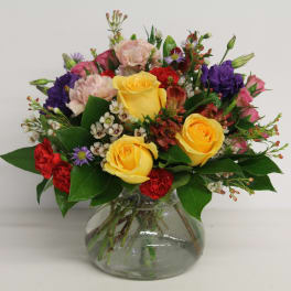 Mixed bouquet of yellow, pink, red, and purple flowers in a glass vase