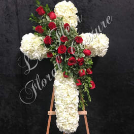 Cross-shaped floral tribute with red roses and white hydrangeas on an easel