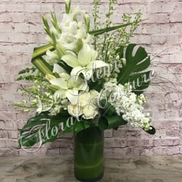 White floral arrangement in a tall green vase with large tropical leaves