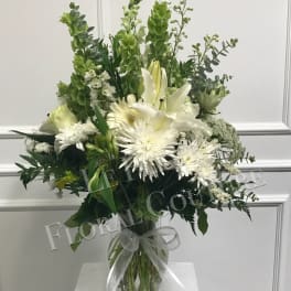 White and green floral arrangement in a glass vase with a ribbon