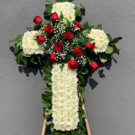 Cross-shaped floral tribute with white chrysanthemums and red roses on an easel