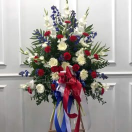 Tall standing floral spray with red, white, and blue flowers on an easel.