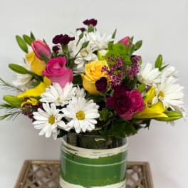 Mixed bouquet of roses, daisies, lilies, and carnations in a glass vase