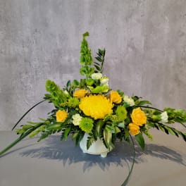 Yellow and green floral arrangement in a white container with a small frog figurine