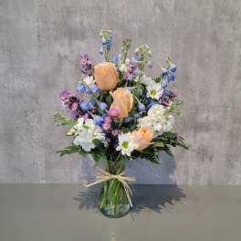 Peach roses and blue-white mixed flowers in a glass vase with a ribbon