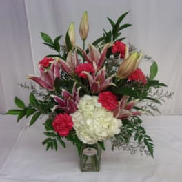 Pink lilies and red carnations in a glass vase with white hydrangea