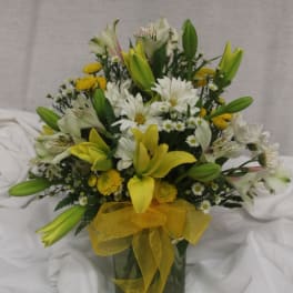 Yellow lilies and white daisies in a glass vase with a yellow ribbon