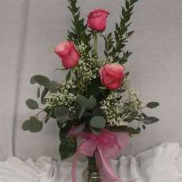 Pink roses in a glass vase with baby's breath and a pink ribbon