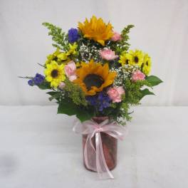Bouquet of sunflowers, pink roses, and blue flowers in a glass vase